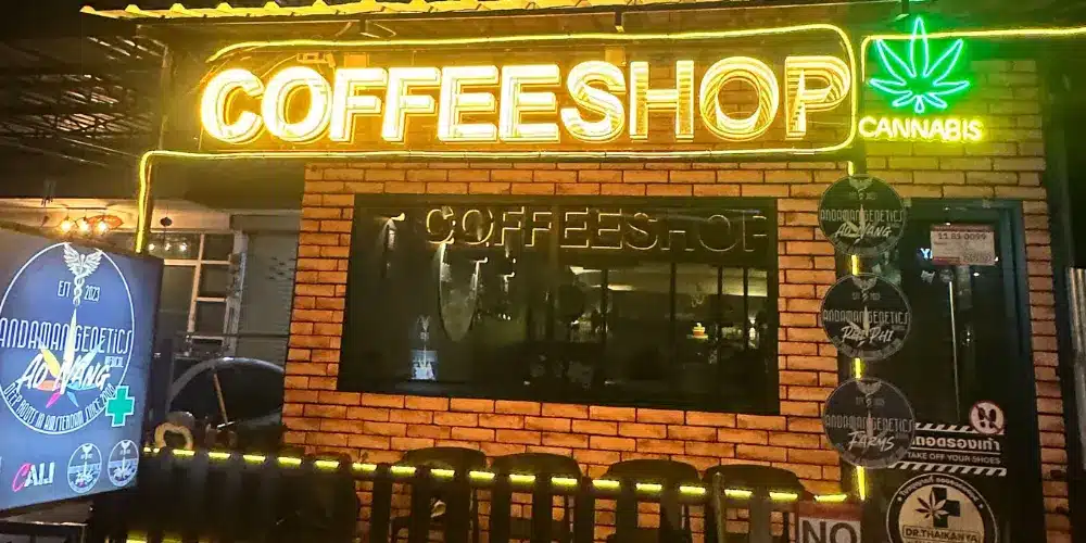 Visitors relaxing outside Andaman Genetics coffeeshop and social club in Ao Nang, Krabi, with outdoor seating, illuminated signage and colourful neon lights at night.