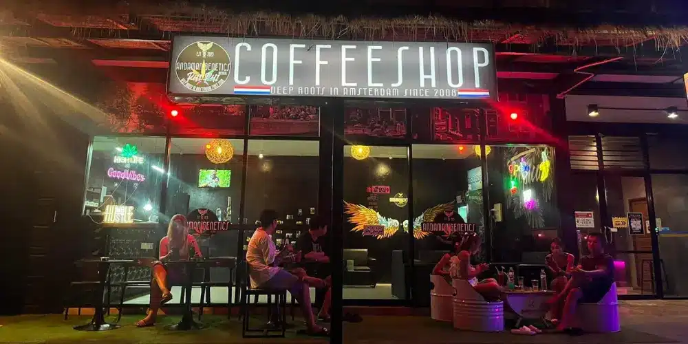 Exterior of Andaman Genetics cannabis dispensary and social club on Koh Phi Phi, Thailand, featuring illuminated coffeeshop signage, outdoor seating and visitors relaxing at night.