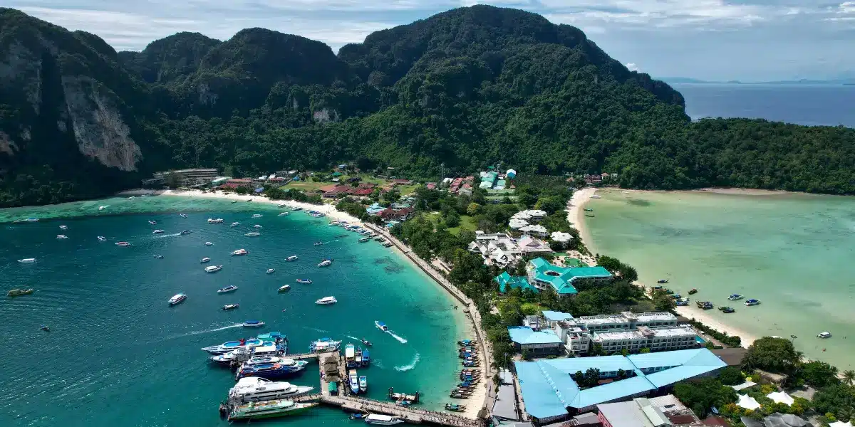 Aerial view of Koh Phi Phi Don, Thailand, showing Ton Sai Bay, Loh Dalum Bay, turquoise waters, longtail boats and tropical limestone mountains.